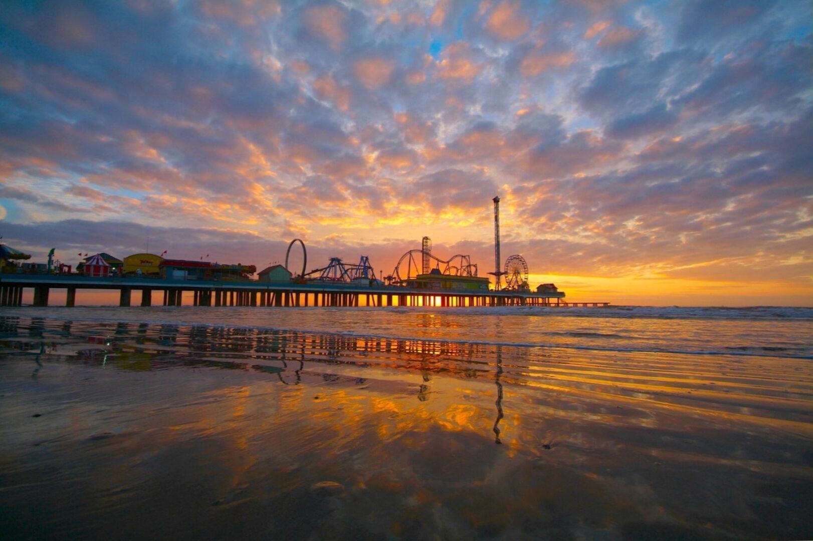 A pier with amusement rides and a Ferris wheel during sunset.