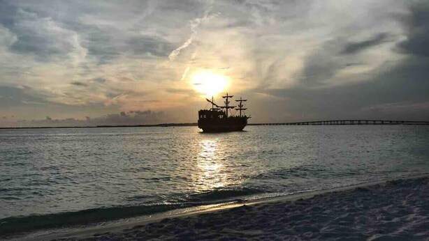 Ein Schiff auf ruhigem Wasser, im Hintergrund ein Sonnenuntergang.