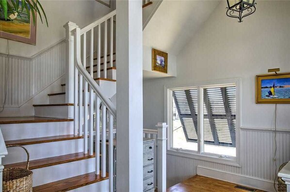 A staircase with white railings and wooden steps, a window with shutters, and a wall-mounted picture. - Nash Cottage-Oceanside Home on Ocean Ridge (Atlantic Beach)