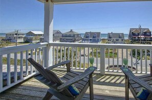 A wooden deck with two lounge chairs and a table, overlooking a beach with houses in the background. - Nash Cottage-Oceanside Home on Ocean Ridge (Atlantic Beach)