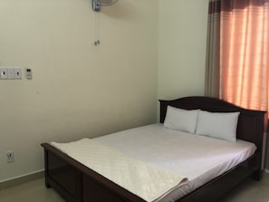 A single bed with a wooden frame and white bedding in a room with beige walls and a power outlet.
