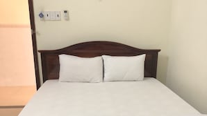 A single-bed room with a wooden headboard, white bedding, and a plain wall with a light switch and a power outlet. - Hong Ngoc Hotel (Ho Chi Minh City)