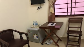 A room with a wooden chair, a small table with a remote control, and a refrigerator with beverages and a glass. - Hong Ngoc Hotel (Ho Chi Minh City)