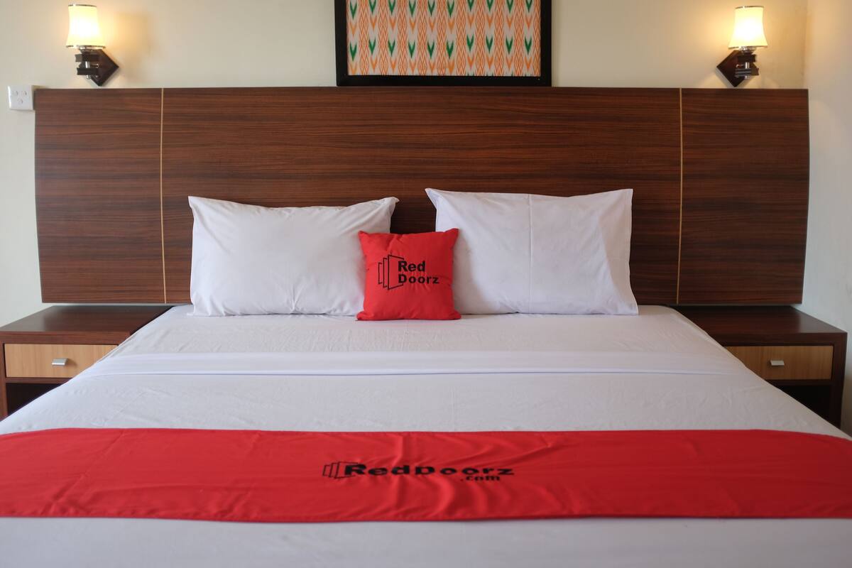 A neatly made bed with white linens and a red blanket, a wooden headboard, and two bedside lamps.