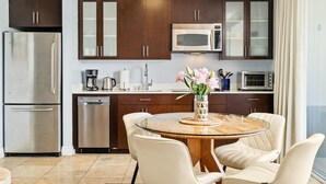 Une cuisine moderne dotée d’appareils électroménagers en acier inoxydable, de meubles de rangement en bois foncé et d’une table ronde en verre, accompagnée de chaises blanches.