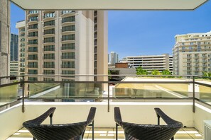 Un balcon avec deux fauteuils en osier, une balustrade en verre et une vue sur les immeubles de grande hauteur.