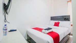 Habitación de hotel con cama, escritorio, botella de agua y televisor montado en la pared.