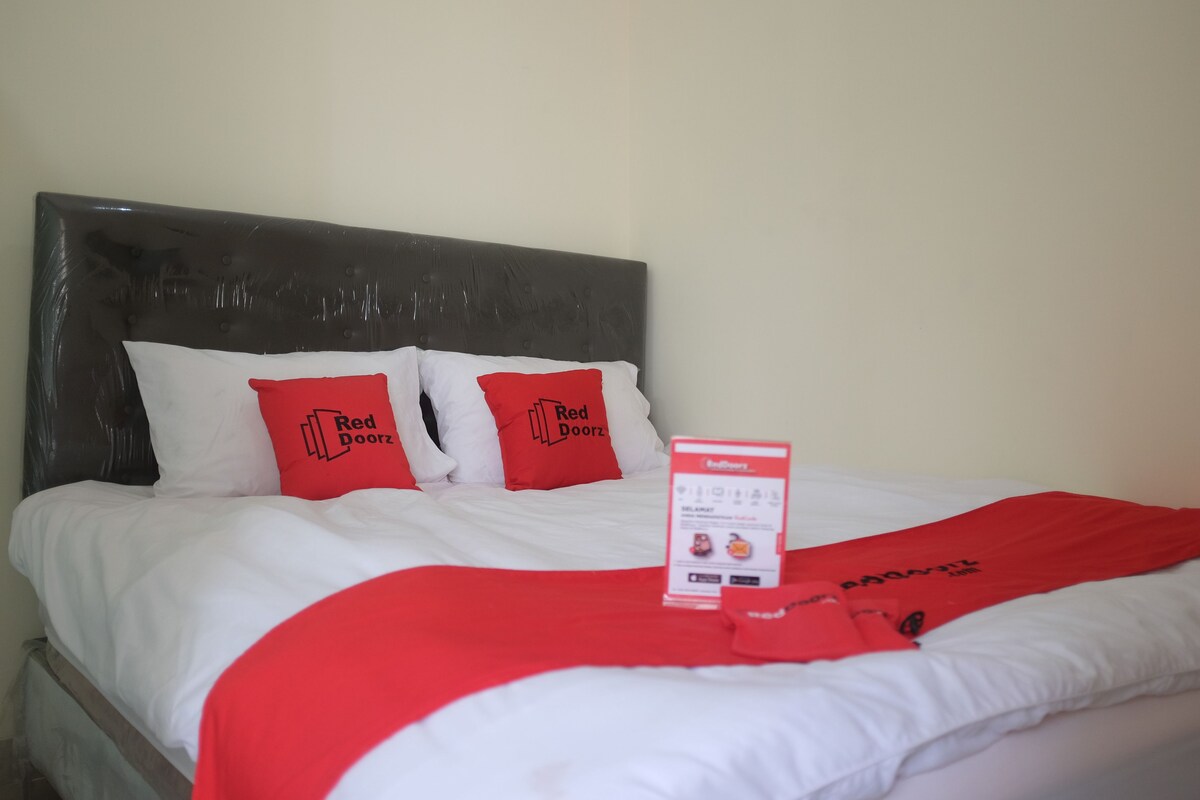 Una cama con ropa blanca y dos almohadas rojas con la marca 'Red Doorz'.