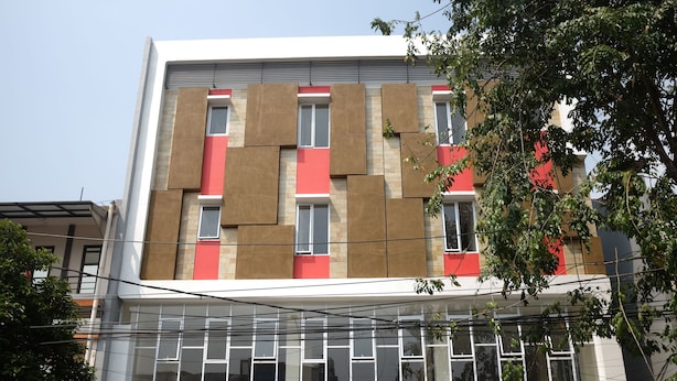 Un edificio de varios pisos con un diseño arquitectónico moderno, que presenta una combinación de paneles beige y rojos, ventanas grandes y líneas eléctricas visibles.