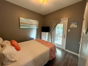 A bedroom with a bed, a dresser, a painting, a television, and a door leading to a balcony.