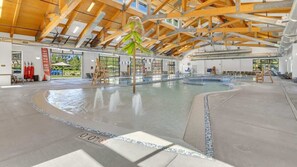 Piscina interior com teto de madeira alto, paredes de vidro transparente e chão revestido com azulejos.