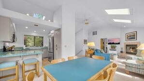 Un vaste espace de vie comprenant un coin repas avec une table et des chaises bleues, une cuisine avec un bar pour prendre le petit-déjeuner et une cheminée.