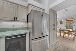 A modern kitchen with stainless steel appliances, light-colored cabinetry, and a dining area with wooden chairs and a table.