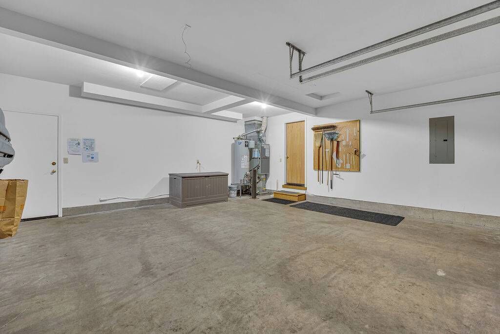 Een ruime, goed verlichte kamer met een betonnen vloer, een groot grijs kastmeubel en een houten deur met treden die leiden naar een zolderruimte.
