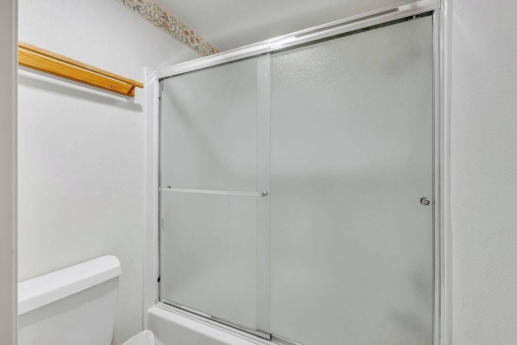 A bathroom with a white toilet, a shower enclosure, and a wooden shelf above the toilet.
