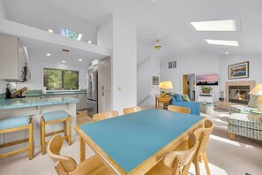 A modern kitchen with a dining area, a living room with a fireplace, and a large window.