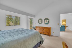 A bedroom with a large bed, a wooden dresser, and two framed botanical prints on the wall.