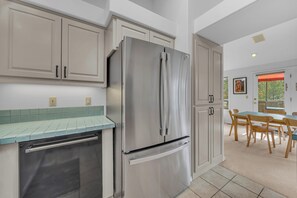 A modern kitchen with stainless steel appliances, light-colored cabinetry, and a dining area with wooden chairs.
