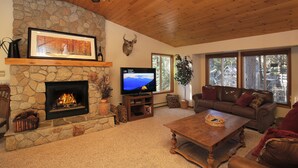 A cozy living room with a stone fireplace, a television, a comfortable couch, and large windows. - Make Memories in Marla Bay, Private Homeowners Beach, 8 Guests (Zephyr Cove)