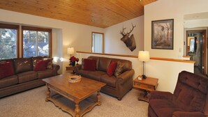 A cozy living room with a wooden ceiling, a brown leather sofa set, a wooden coffee table, and a mounted deer head on the wall. - Make Memories in Marla Bay, Private Homeowners Beach, 8 Guests (Zephyr Cove)