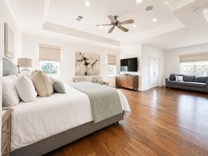 A spacious bedroom with a large bed, a ceiling fan, and a TV mounted on the wall.