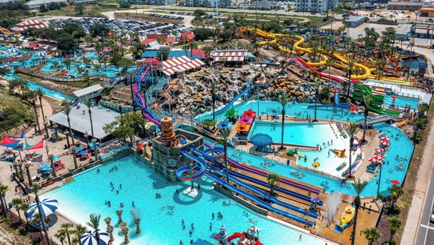 An aerial view of a water park with multiple pools, slides, and a large central pool area.
