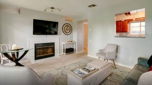 Un salon avec une cheminée, un téléviseur, une horloge et une fenêtre ornée d’un rideau rouge.
