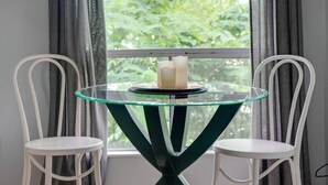 Une pièce avec une table à plateau de verre placée au centre, sous une fenêtre, et flanquée de deux chaises blanches.