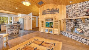 A spacious living area with a stone fireplace, wooden ceiling, and a large TV. - Single level Sunriver rental, large deck, hot tub (Sunriver)
