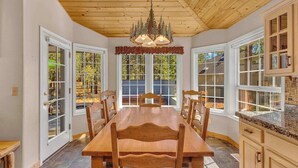 A dining area with a wooden table and chairs, large windows, and a chandelier. - Single level Sunriver rental, large deck, hot tub (Sunriver)