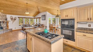 A spacious kitchen with granite countertops, wooden cabinets, and a large island with a stove. - Single level Sunriver rental, large deck, hot tub (Sunriver)