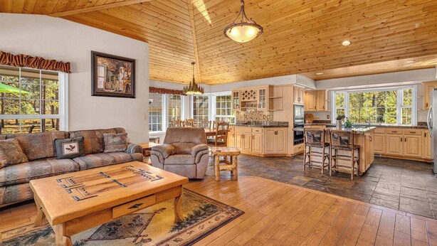 A spacious living area with a wooden ceiling, a sofa, a coffee table, and a kitchen with wooden cabinets and a large window. - Single level Sunriver rental, large deck, hot tub (Sunriver)