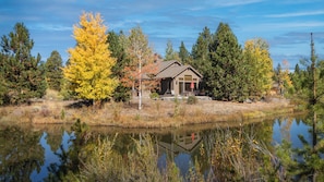 A cabin with a deck, surrounded by trees and a body of water.