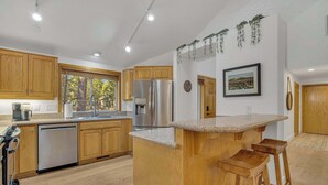 A modern kitchen with wooden cabinets, stainless steel appliances, and a central island with stools. - Hot Tub, AC, Ping Pong, Foosball, 4bdrm, Family (Bend)