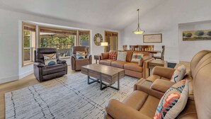 A spacious living room with leather sofas, a recliner, and a coffee table. Large windows offer a view of the outdoors. - Hot Tub, AC, Ping Pong, Foosball, 4bdrm, Family (Bend)