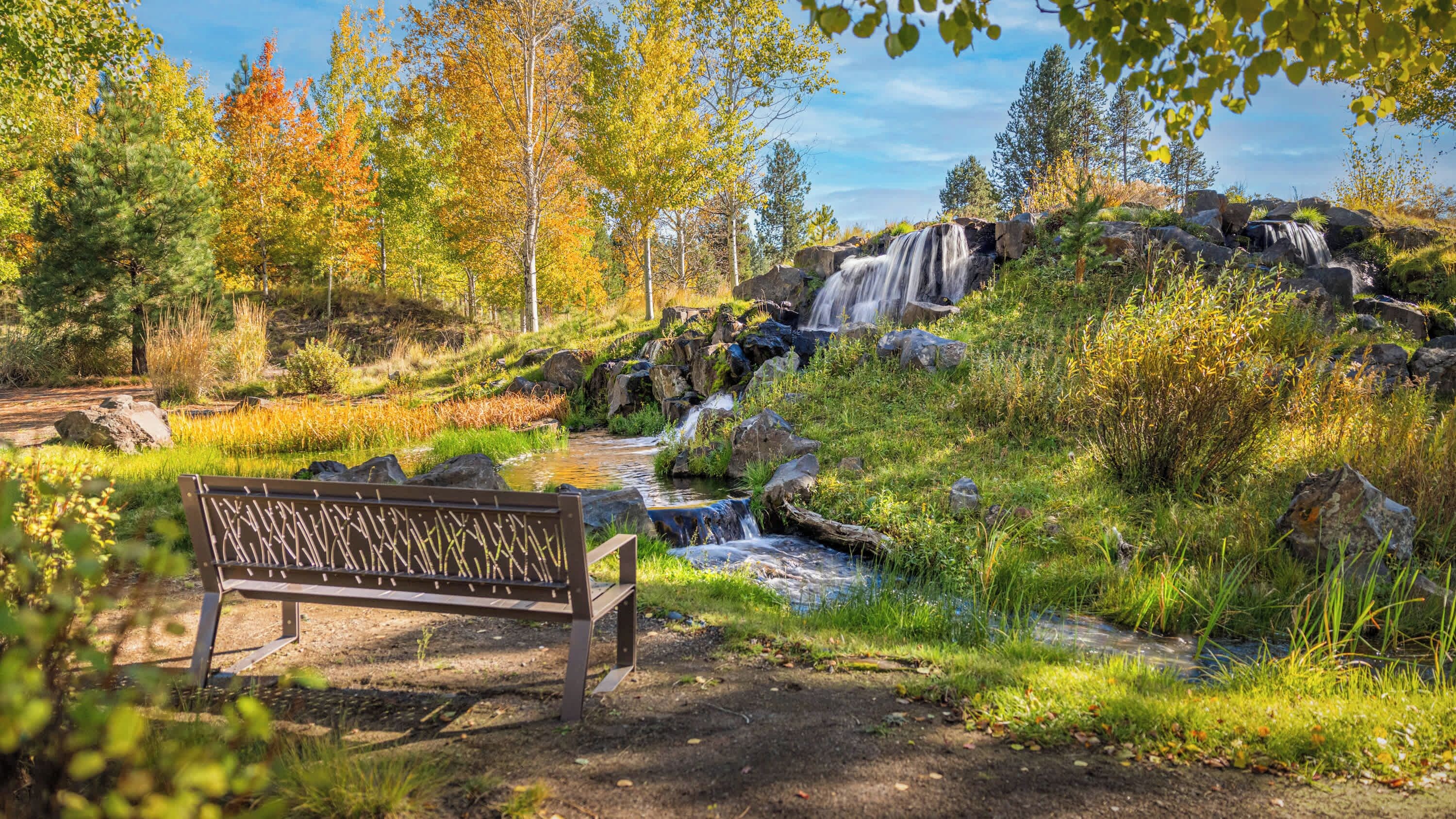 A bench in a natural setting with a waterfall and trees.