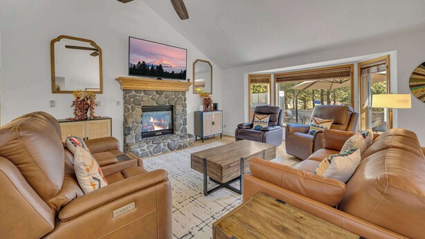 A living room with leather sofas, a stone fireplace, a ceiling fan, and a large window. - Hot Tub, AC, Ping Pong, Foosball, 4bdrm, Family (Bend)
