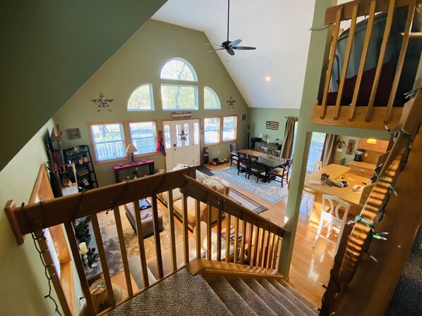 A spacious loft-style room with a high ceiling, large windows, and a staircase leading to an upper level.