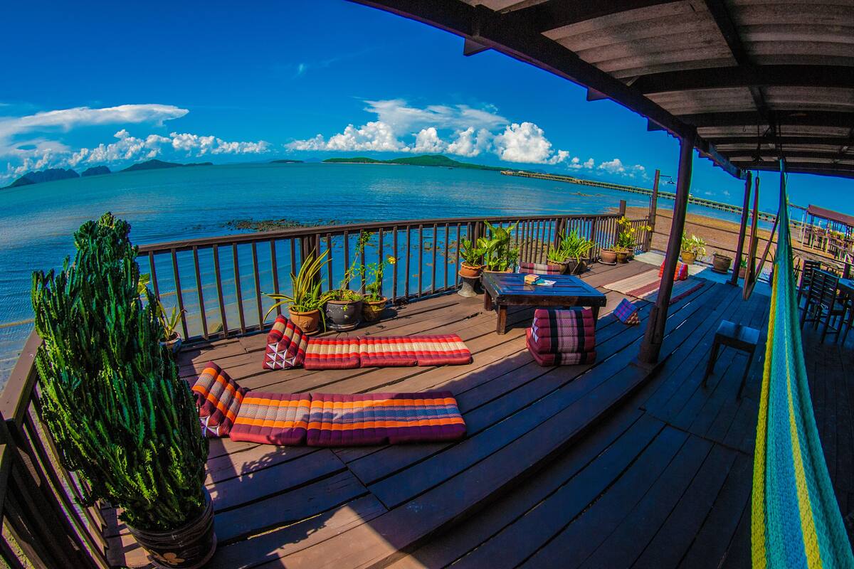 Una terraza de madera con sillones de descanso, plantas en macetas y vistas al océano y a islas distantes.