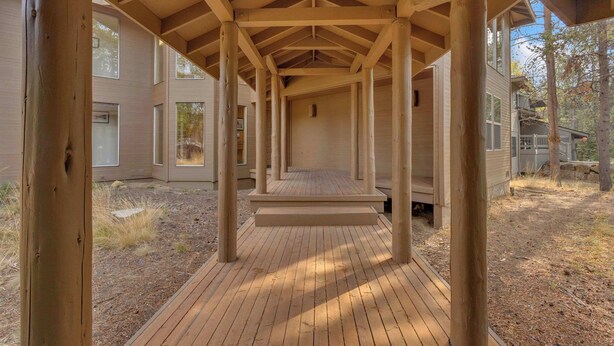 A covered wooden deck with a simple, open design, surrounded by a building with large windows and a natural landscape. - Unique, spacious, private deck, HT, great room (Sunriver)