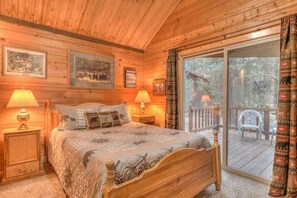 Ein Schlafzimmer einer Holzhütte mit einem Bett, zwei Nachttischlampen und einem großen Fenster mit Blick ins Freie.