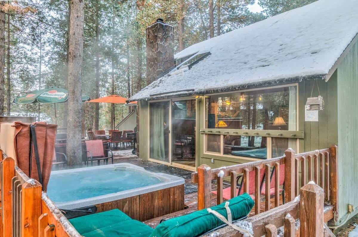 A cabin with a hot tub, wooden deck, and outdoor seating area surrounded by trees.