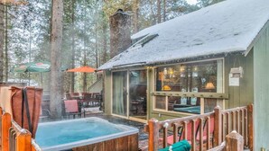 Eine Holzhütte mit Whirlpool, einer Holzterrasse und einer Sitzgelegenheit im Freien, umgeben von Bäumen.