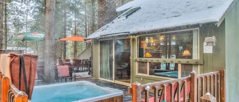 A cabin with a hot tub, wooden deck, and outdoor seating area surrounded by trees.