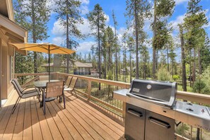 A wooden deck with a grill, chairs, and an umbrella.