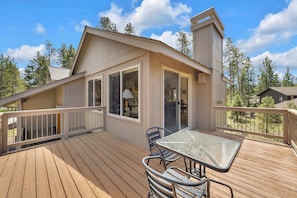 A wooden deck with a table and chairs, a covered area with a lamp, and a view of trees and another building.