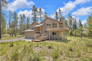 A two-story house with a balcony, surrounded by tall pine trees.