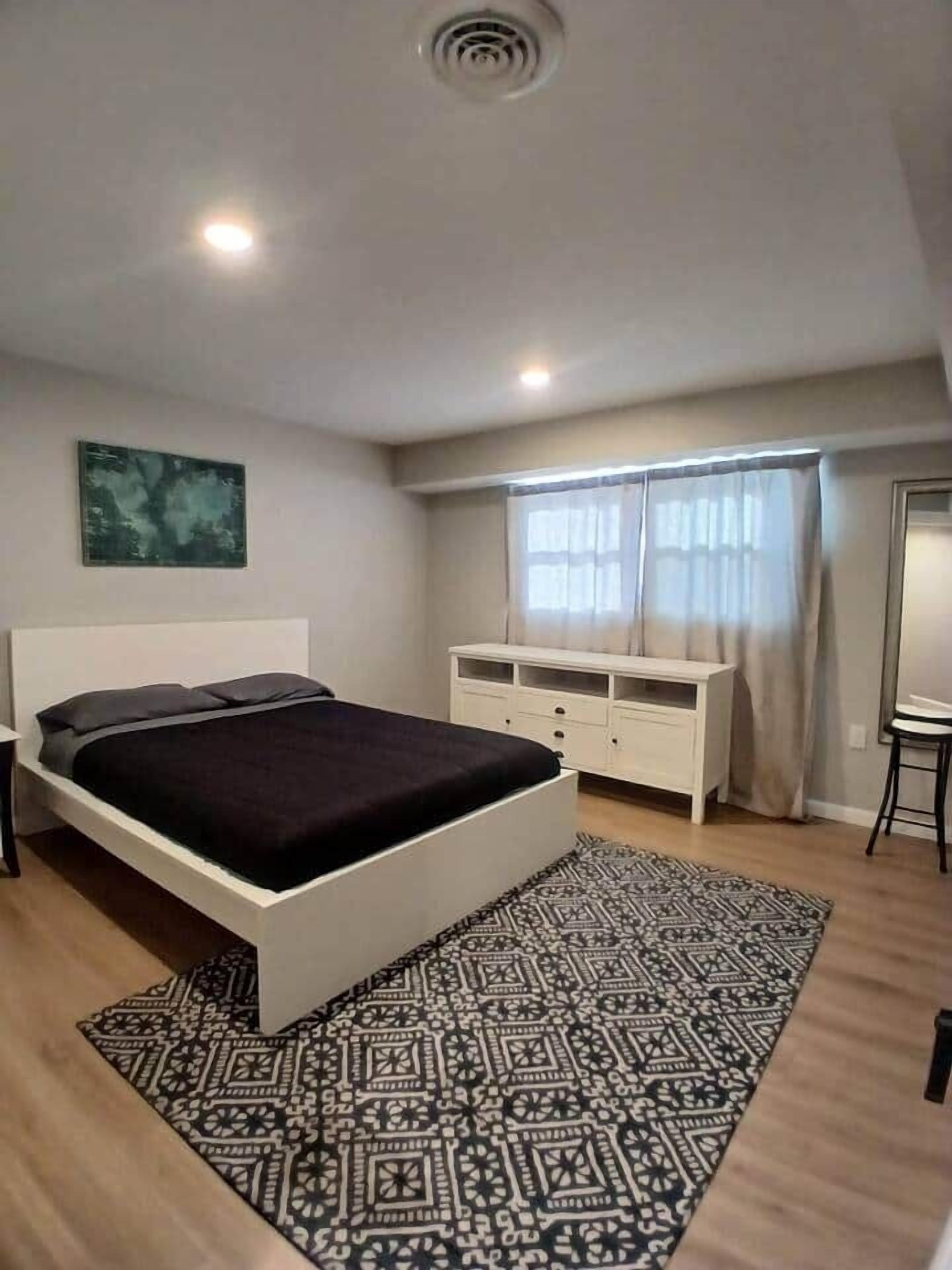 Quarto com cama, penteadeira, espelho e janela com cortinas.