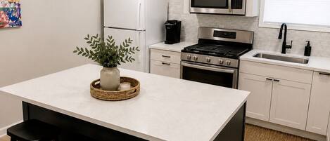 Una cocina moderna con una isla central, taburetes de bar, microondas, estufa, horno y armarios blancos.