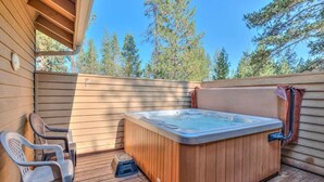 Een houten terras met een jacuzzi, twee stoelen en een klein trapje dat naar het terras leidt.